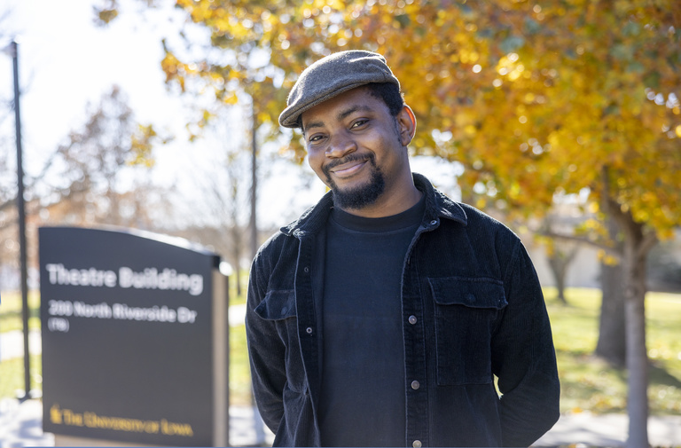 Sixtus Chetachi “Cheta” Igbokwe, a second-year Theatre Arts MFA student in playwriting, smiles in front of UI Theatre Building Sign