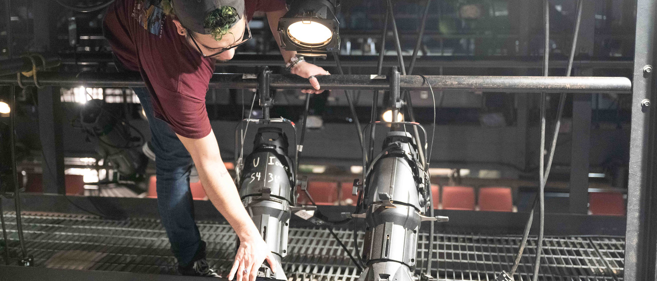 a lighting design student adjusts a stage lighting fixture in Thayer Theatre