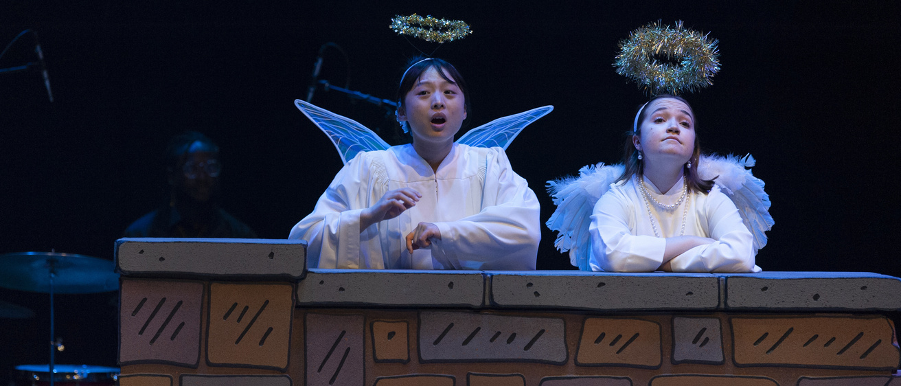 undergraduate actors dressed in angel costumes and sitting behind a brick wall, from the play Smile Medicine