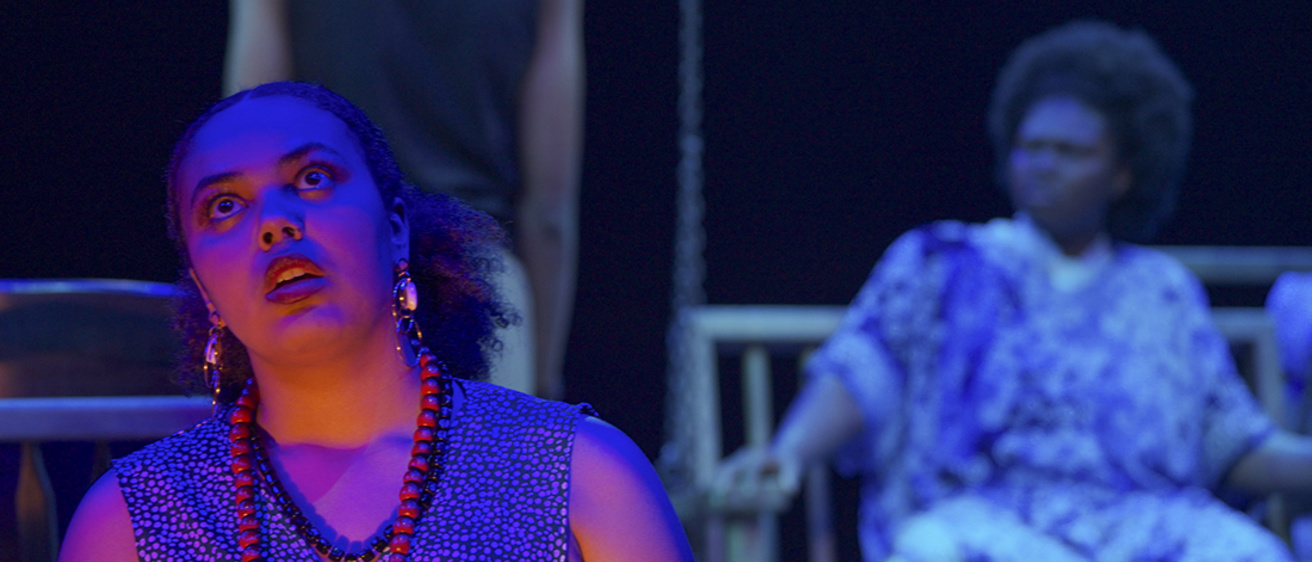 Video still of an actor from In the Red and Brown Water by Tarell Alvin McCraney looking upwards longingly in purple and orange light