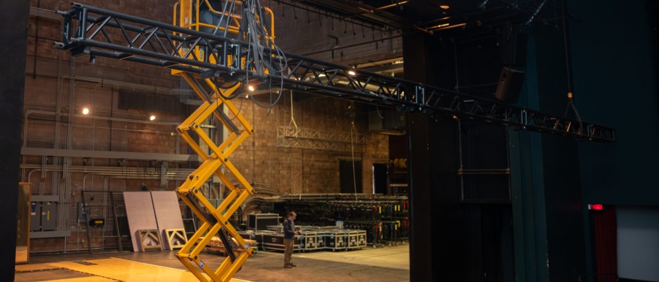 An electrical crew member raises scaffolding to work on the lighting system above at the University of Iowa Theatre Building in Iowa City, Iowa on Dec. 1, 2025. The department is currently working on sets for their upcoming show How to Defend Yourself which will have its first performance on February 6, 2026.
