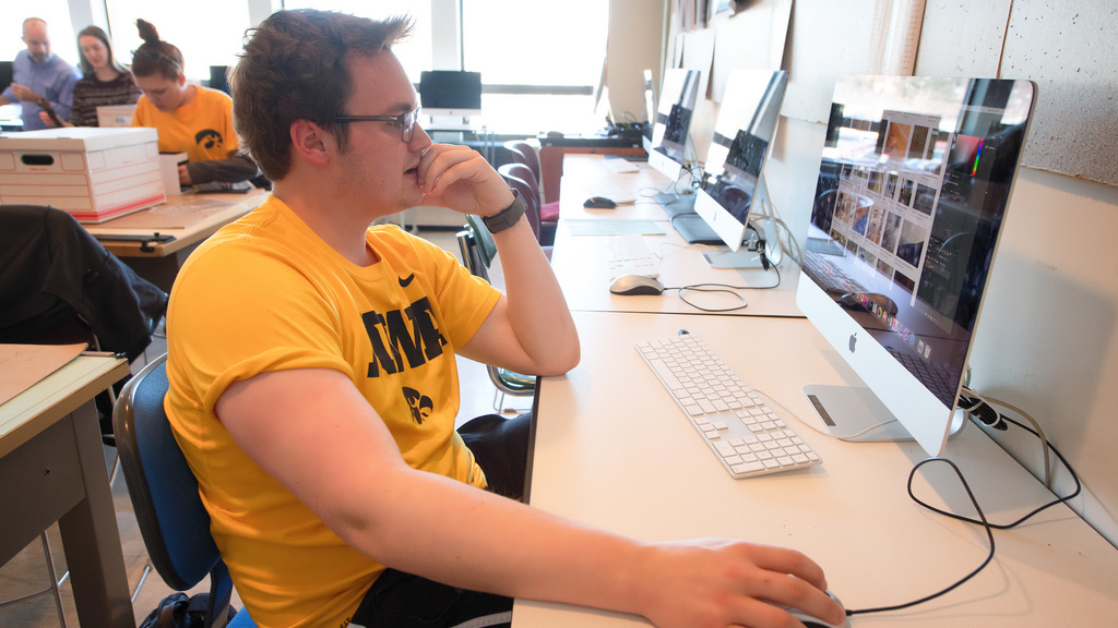 Theatre student in a Hawkeye t-shirt working at an iMac computer in a sunny computer studio