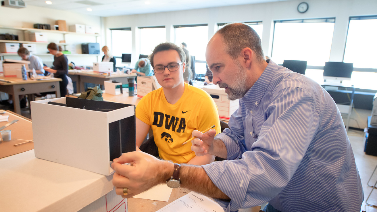 Faculty member Eric Stone instructs an undergraduate student wearing an Iowa Hawkeyes T-shirt, in his scenery design classroom